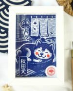 Linogravure bleue d’un chien Akita endormi dans un panier sur un tatami, avec un noren flottant et un furin suspendu en arrière-plan