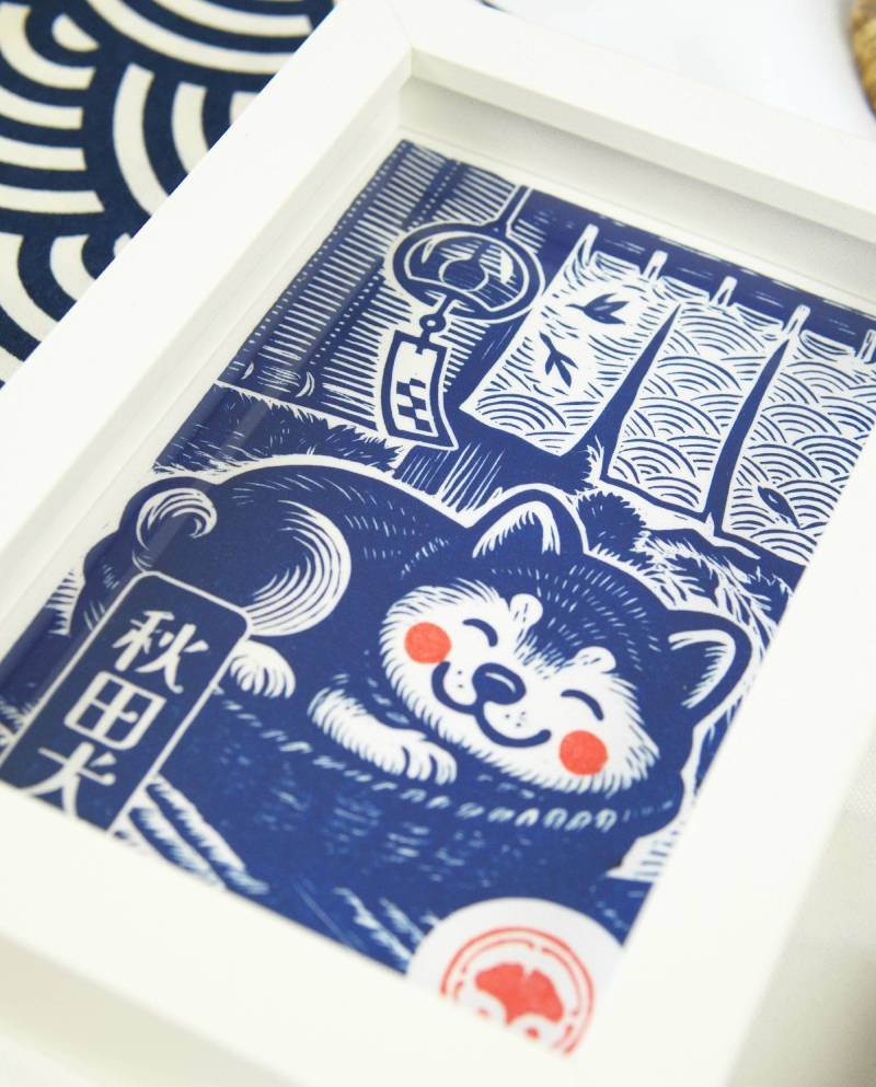 Linogravure bleue d’un chien Akita endormi dans un panier sur un tatami, avec un noren flottant et un furin suspendu en arrière-plan