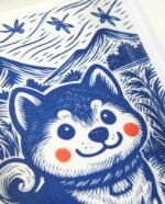 Linogravure bleue d’un chien Akita assis dans un champ, vu de trois quarts, avec des montagnes japonaises et des libellules en arrière-plan
