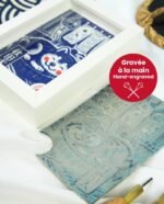 Linogravure bleue d’un chien Akita endormi dans un panier sur un tatami, avec un noren flottant et un furin suspendu en arrière-plan
