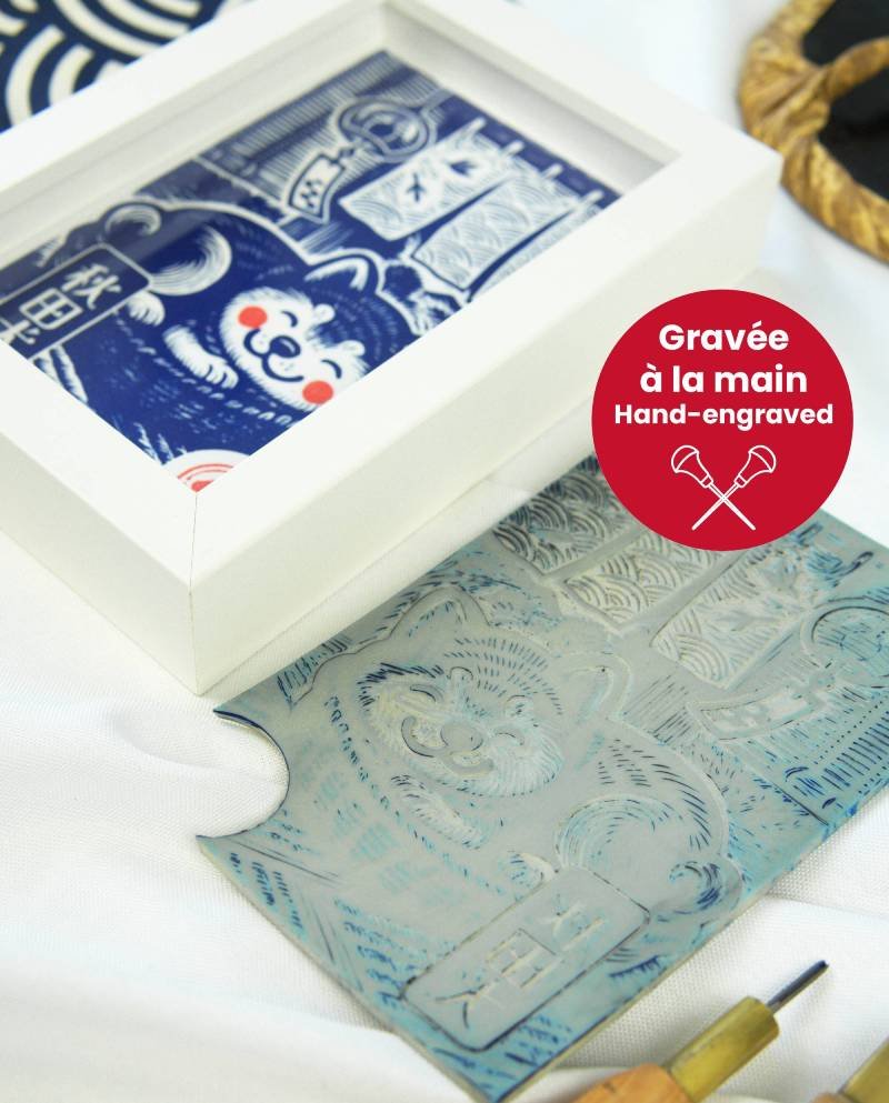 Linogravure bleue d’un chien Akita endormi dans un panier sur un tatami, avec un noren flottant et un furin suspendu en arrière-plan